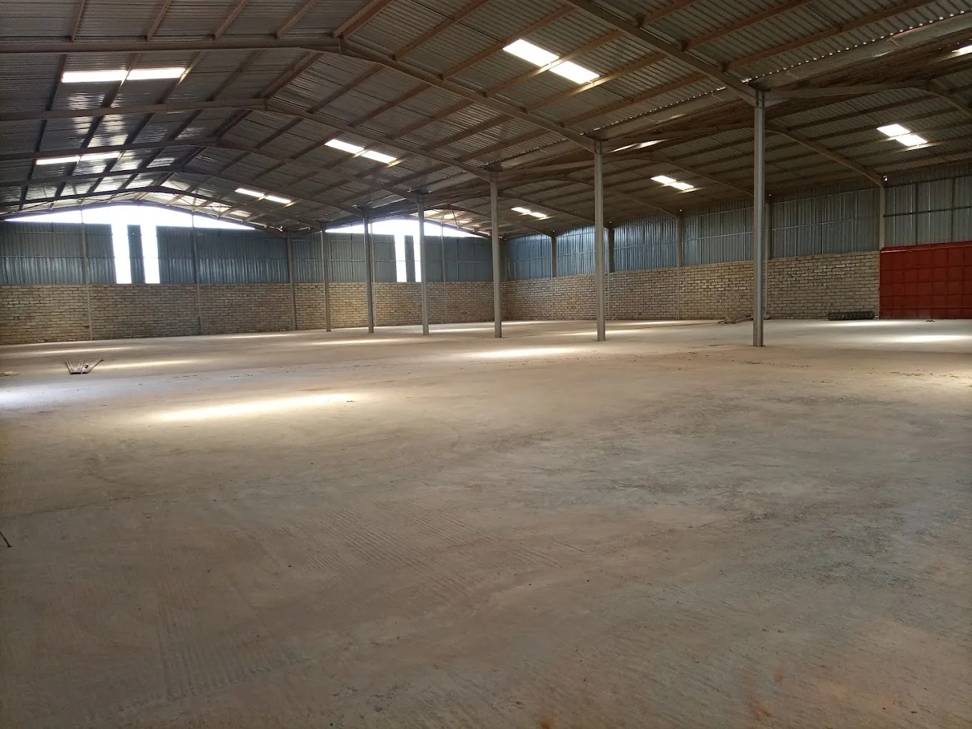 Kampala warehouse interior with clear-span storage space ready for short-term tenant occupation, showing roller shutter doors and concrete floor.